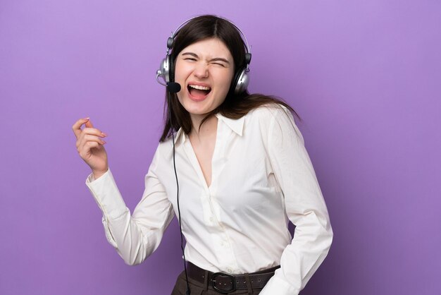 Telemarketer mujer rusa trabajando con un auricular aislado sobre fondo púrpura haciendo gesto de guitarra