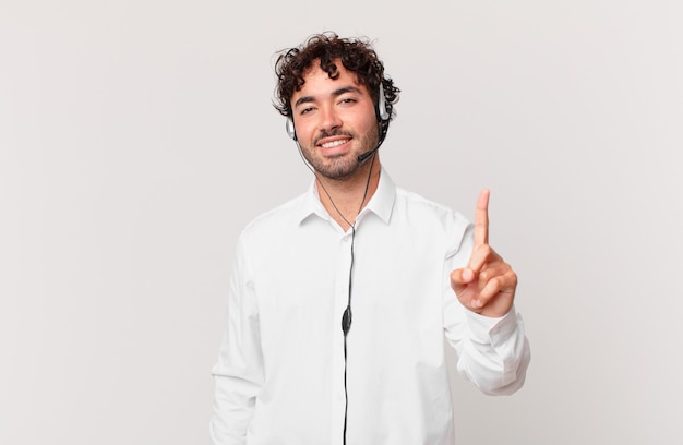 Telemarketer sonriendo y luciendo amigable, mostrando el número uno o el primero con la mano hacia adelante, contando hacia atrás