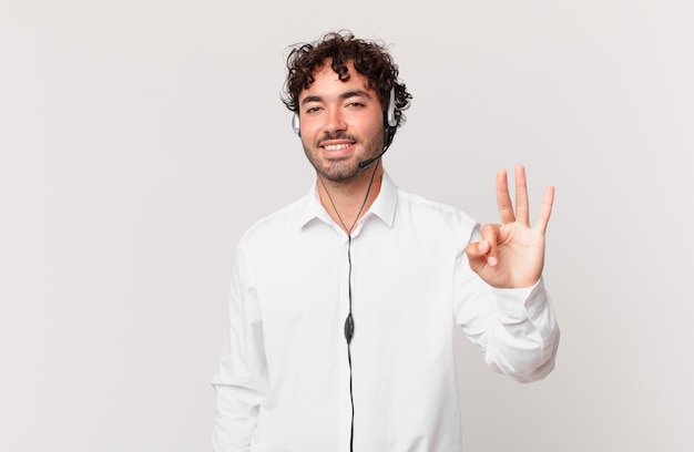 Telemarketer sonriendo y mirando amigable, mostrando el número tres o tercero con la mano hacia adelante, contando hacia atrás