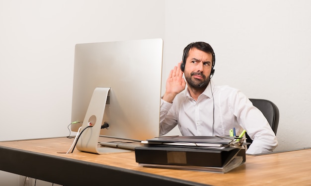 Telemarketermann in einem Büro hörend auf etwas, indem er Hand auf das Ohr setzt