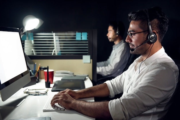 Telemarketers de atendimento ao cliente asiático masculino trabalhando turno da noite em call center