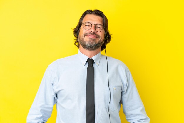 Telemarketing holandês trabalhando com um fone de ouvido isolado em um fundo amarelo com óculos e feliz