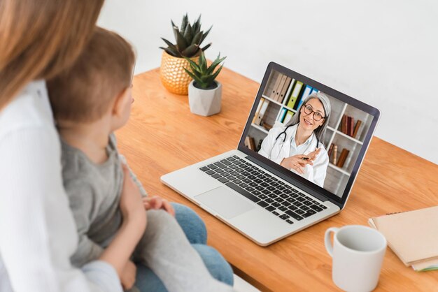 Telemedizin-Konzept Kaukasische Mutter im Mutterschaftsurlaub mit einem Kleinkind, die ein Videokonferenzgespräch mit einem Arzt-Kinderarzt online aus der Ferne auf einem Laptop führt