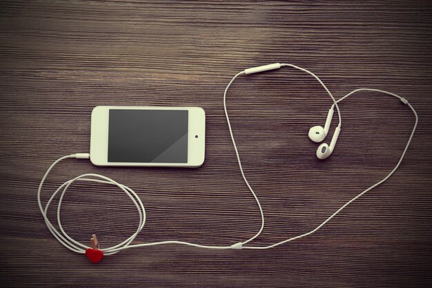 Foto telemóvel e fones de ouvido com coração vermelho em fundo de madeira