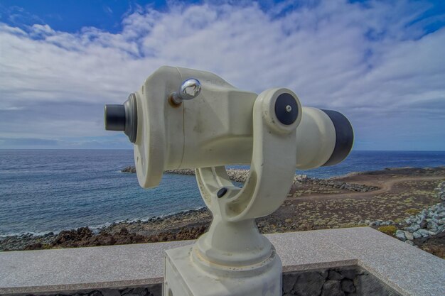 Telescopio que funciona con monedas para la observación de la playa, el cielo azul y las nubes