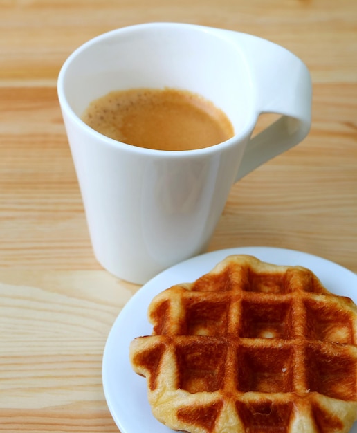 Teller einer belgischen Waffel mit verschwommenem heißem Kaffee im Hintergrund