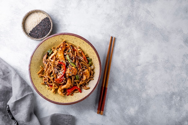 Teller mit asiatischen Buchweizen-Soba-Nudeln mit Gemüse, Pilzen und Hühnchen auf hellgrauem Hintergrund