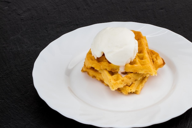 Teller mit belgischen Waffeln mit Eis auf dunklem Hintergrund.