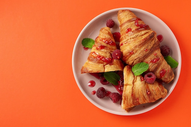 Teller mit Croissants mit Himbeermarmelade auf orangem Hintergrund