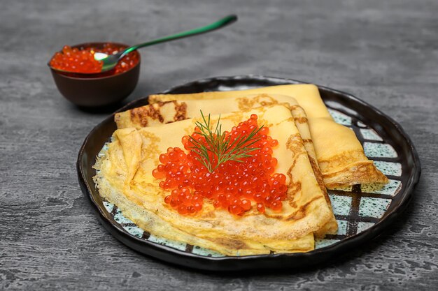 Teller mit dünnen Pfannkuchen und rotem Kaviar auf dem Tisch
