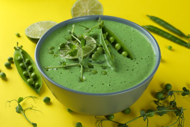 Teller mit Erbsensuppe und Zutaten auf gelber Oberfläche