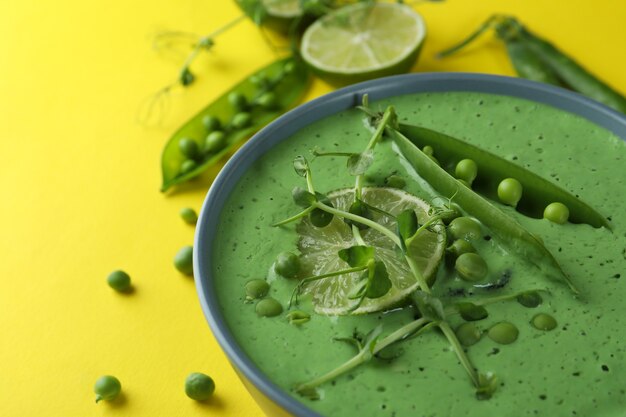 Teller mit Erbsensuppe und Zutaten auf gelber Oberfläche