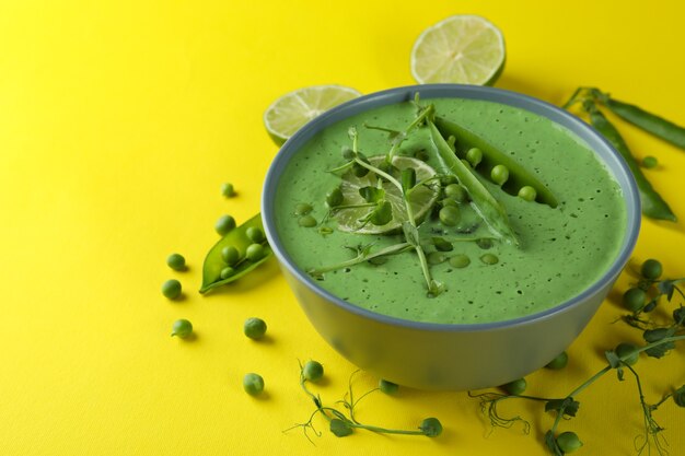 Teller mit Erbsensuppe und Zutaten auf gelber Oberfläche