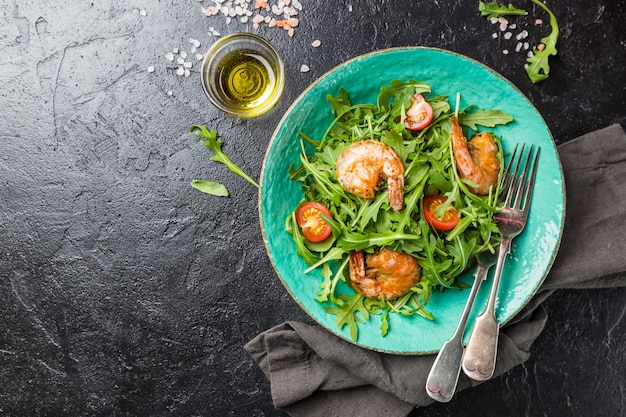 Teller mit frischem Salat mit Rucola oder Salatrakete, Garnelen und Tomate, Draufsicht. Konzepte für gesunde Ernährung.