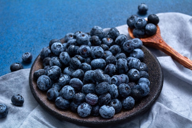 Teller mit frischen Heidelbeeren auf blauem Grund. Frische Beeren und Holzlöffel