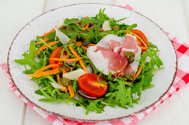 Teller mit frischen Salatblättern, Parmesanscheiben und Schinken