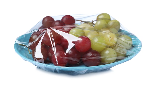 Teller mit frischen Weintrauben, umwickelt mit transparenter Kunststoff-Stretchfolie, isoliert auf weiß
