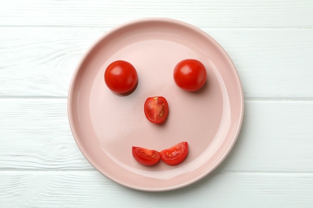 Teller mit fröhlichem Gesicht aus Tomate auf weißem Holz