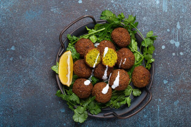 Teller mit gebratenen Falafelbällchen, serviert mit frischem grünen Koriander und Zitrone Draufsicht auf rustikalem Betonhintergrund Traditionelles veganes Gericht der Küche des Nahen Ostens