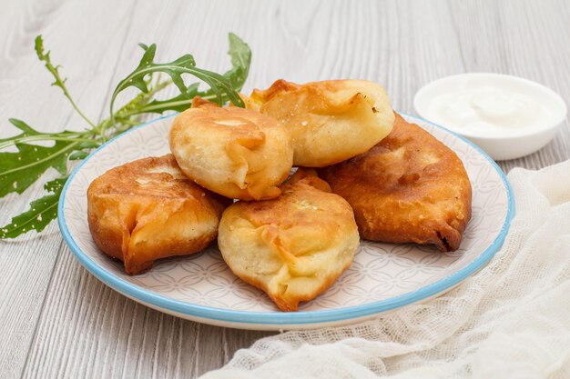 Teller mit gebratenen Kuchen, Schüssel mit Sauerrahm, Stück weißem Stoff und Grüns auf grauen Brettern.