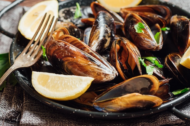 Teller mit gedämpften Muscheln mit Zitrone und Petersilie auf einem rustikalen Holztisch.