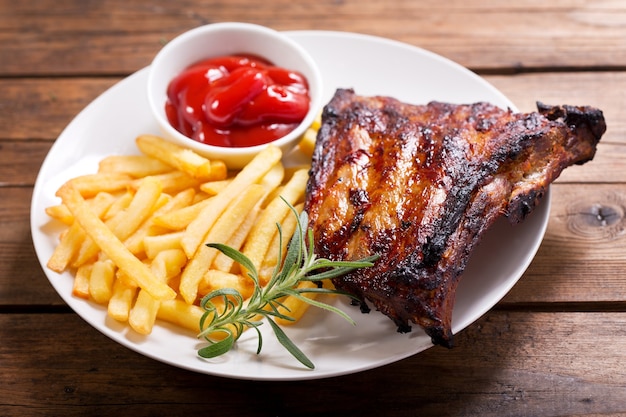 Teller mit gegrillten Schweinerippchen mit Pommes Frites auf Holztisch