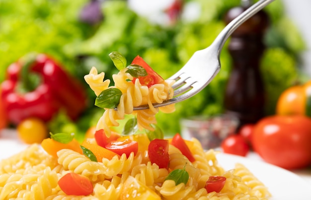 Teller mit gekochten italienischen Fusilli-Nudeln mit Tomaten und Basilikumblättern