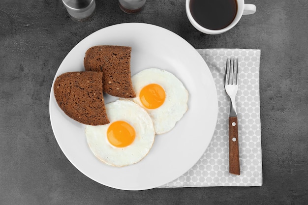 Teller mit hausgemachten Spiegeleiern mit Brot und einer Tasse Tee auf dem Tisch