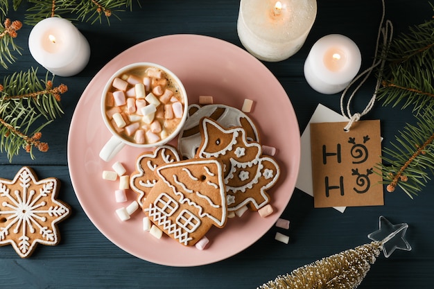 Teller mit hausgemachten Weihnachtsplätzchen, Kaffee, Marshmallows auf Holztisch, auf blau. Draufsicht