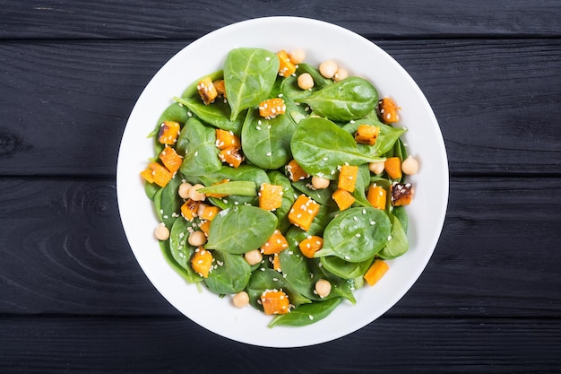 Teller mit Herbstsalat mit Kürbis, Spinat, Kichererbsen und Sesam. Veganer Hintergrund