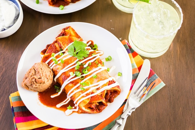 Teller mit Hühnchen-Enchiladas, garniert mit Frühlingszwiebeln und Sauerrahm.