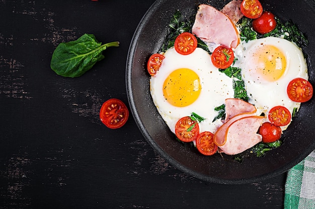 Teller mit Keto-Diät-Essen, gebratenen Eiern, Schinken, Spinat und Tomaten, Keto-Paleo-Frühstück
