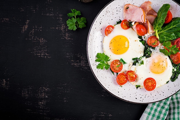 Teller mit Keto-Diät-Essen, gebratenen Eiern, Schinken, Spinat und Tomaten, Keto-Paleo-Frühstück
