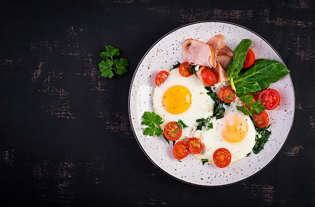 Teller mit Keto-Diät-Essen, gebratenen Eiern, Schinken, Spinat und Tomaten, Keto-Paleo-Frühstück