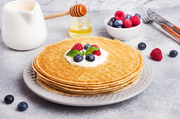 Teller mit köstlichen dünnen Pfannkuchen mit Beeren auf grauem Tisch.