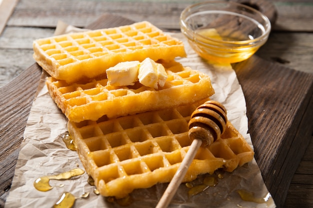 Teller mit leckerem Waffelhonig und einer Scheibe Butter. Auf einem hölzernen Hintergrund. Nahansicht