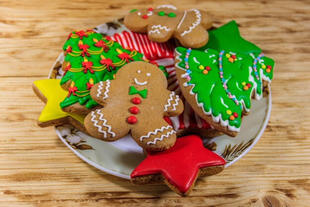 Teller mit leckeren festlichen Weihnachtslebkuchen in Form von Weihnachtsbaum, Lebkuchenmann, Stern und Weihnachtsstrumpf auf Holztisch