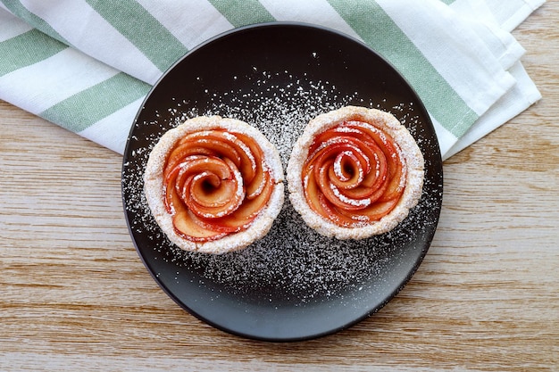 Teller mit leckeren und gesunden Apfel-Mini-Kuchen in Rosenform, bestreut mit Puderzucker