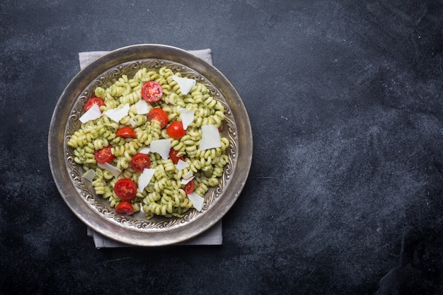 Teller mit Nudel-Fusilli mit Pesto-Sauce und Kirschtomaten auf dunklem Hintergrund