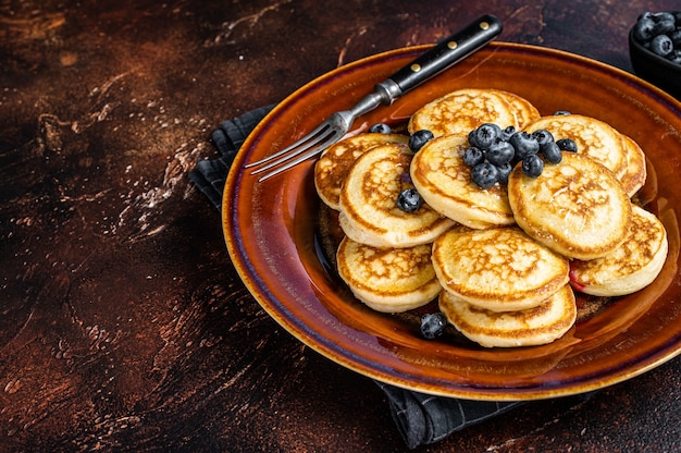 Teller mit Pfannkuchen mit frischen Blaubeeren und Sirup. Dunkler Hintergrund. Ansicht von oben. Platz kopieren.