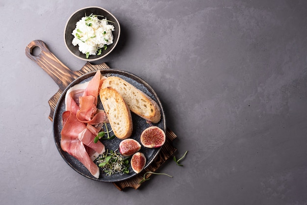 Teller mit Prosciutto Antipasto, Toast, Ricotta auf einem Schneidebrett auf grauem Hintergrund, Schinkensnack.