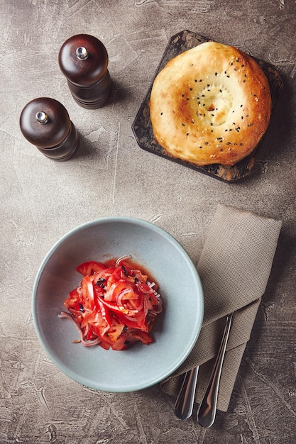 Teller mit Salat aus Tomaten, roten süßen Zwiebeln und Basilikumblättern auf serviertem Tisch mit Besteck