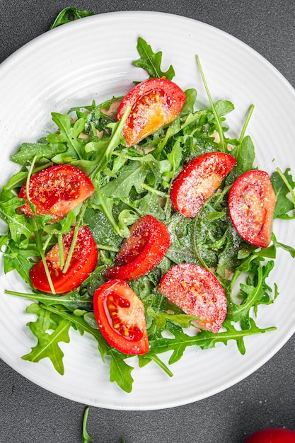 Teller mit Salat, Tomate, Rucola, geriebenem Käse, Olivenöl, gesunde Mahlzeit, Snack auf dem Tisch