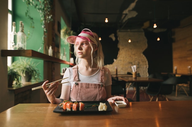 Teller mit Sushi-Rollen im Restaurant mit Frau, die Essstäbchen hält