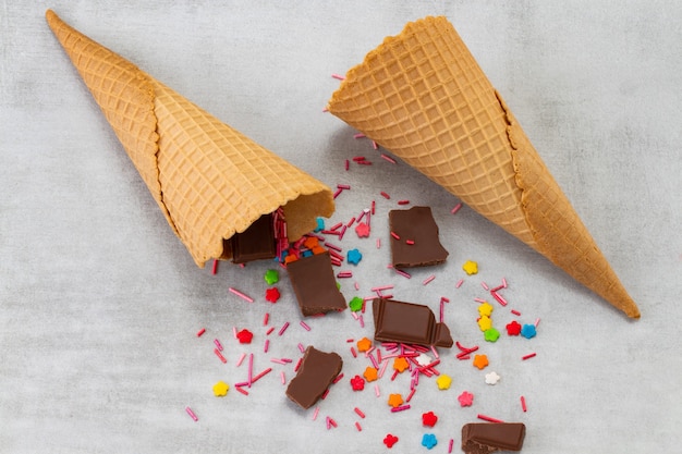 Teller mit Vanille- und Schokoladeneiskugeln mit Schokoladenstückchen und Waffeltüten bestreuen