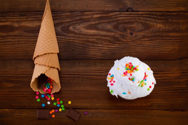 Teller mit Vanilleeisschaufel mit Streuseln und Waffeltüten auf Holz.