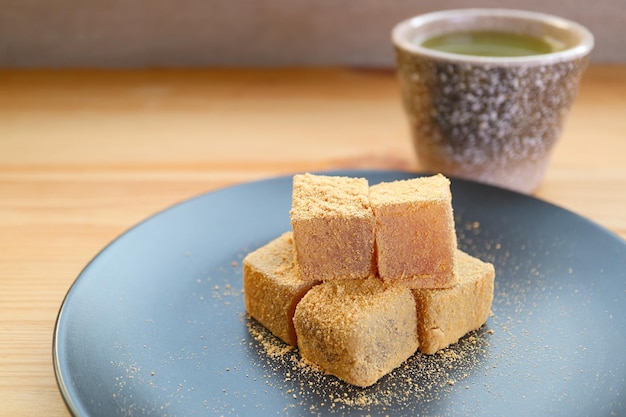 Teller mit Warabimochi, einem traditionellen japanischen Konfekt mit verschwommenem heißem Matcha-Grüntee im Hintergrund