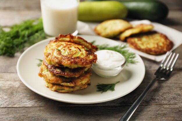 Teller mit Zucchinipfannkuchen und Sauce auf Holztisch