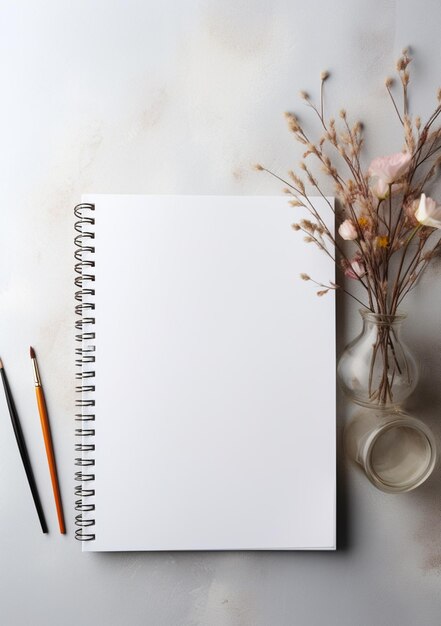 Foto tem um caderno branco com uma caneta e um vaso com flores generativas ai