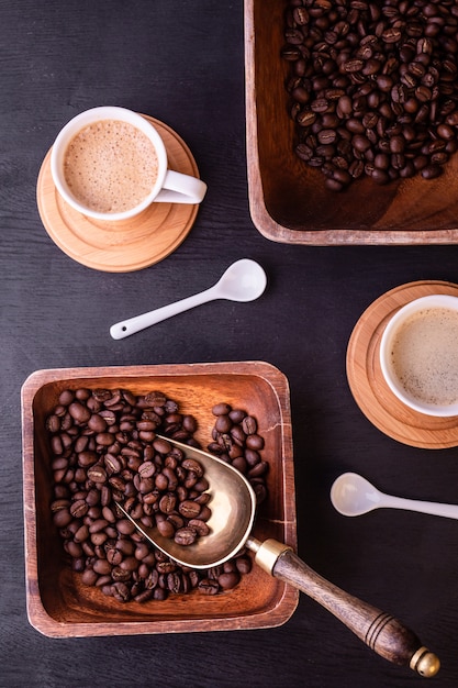 Tema del café Tazas calientes de café y plato con granos de café en la mesa de madera negra.